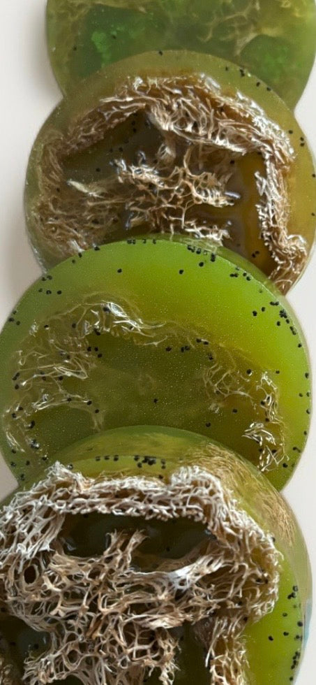 Close up photo of round strawberry guava loofah soap bars with poppyseeds, and green shimmering mica showing texture by the blooming butterfly company