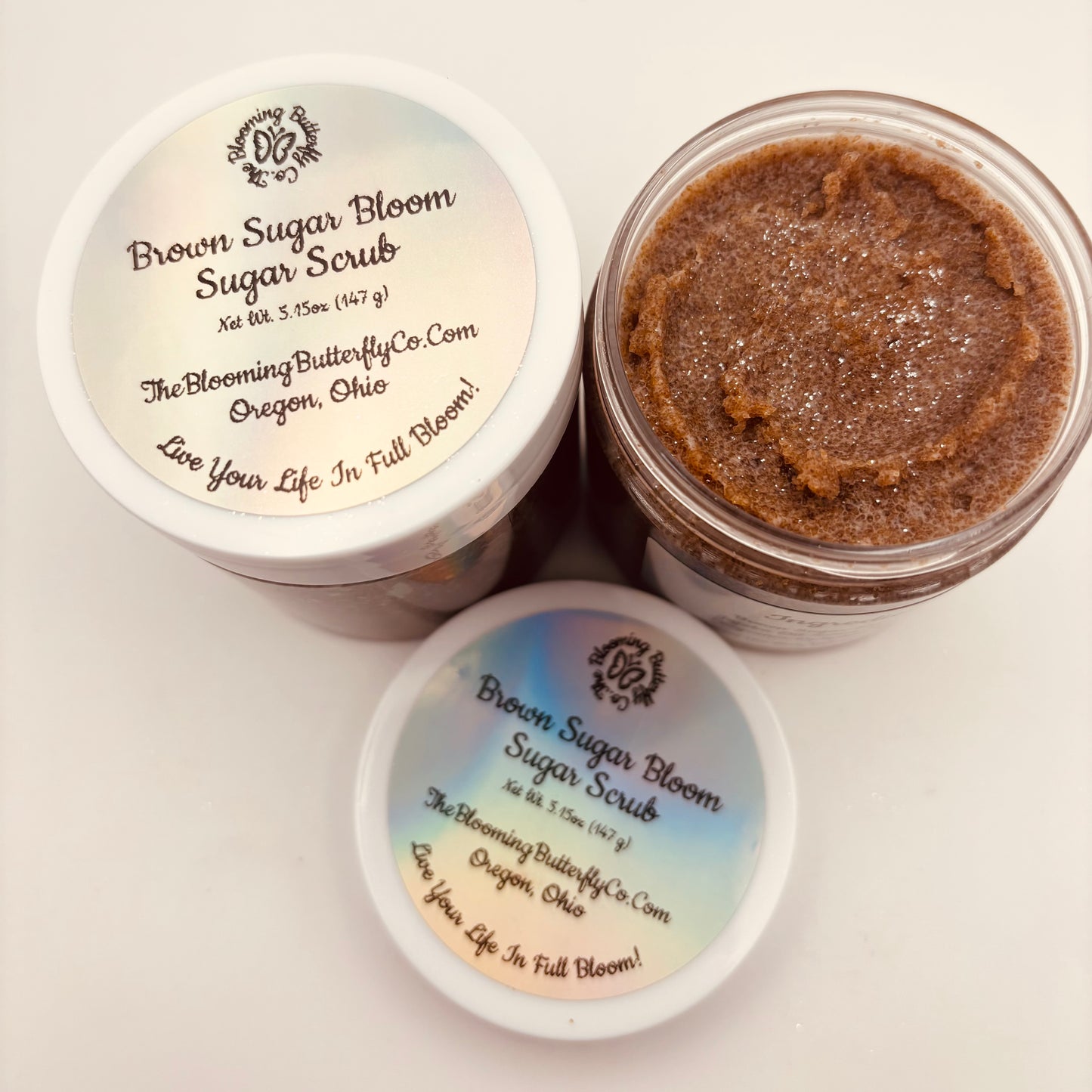 Two containers of Brown Sugar Bloom Sugar Scrub with visible labels on a light background handcrafted by the blooming butterfly Company
