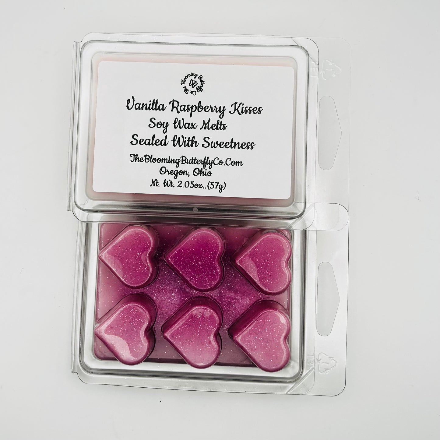 Shimmering Magenta colored wax melts scented in vanilla raspberry fragrance oil in a clear clamshell container shaped in hearts with a white label on a white background