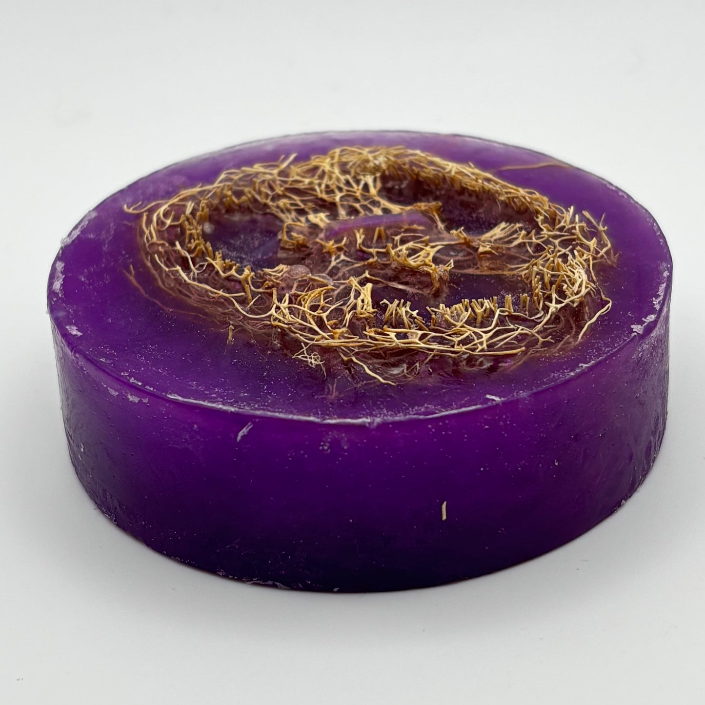 close up photo of a round 4.3oz. of lavender loofah soap bar showing organic loofah texture and shimmering purple mica by the blooming butterfly company