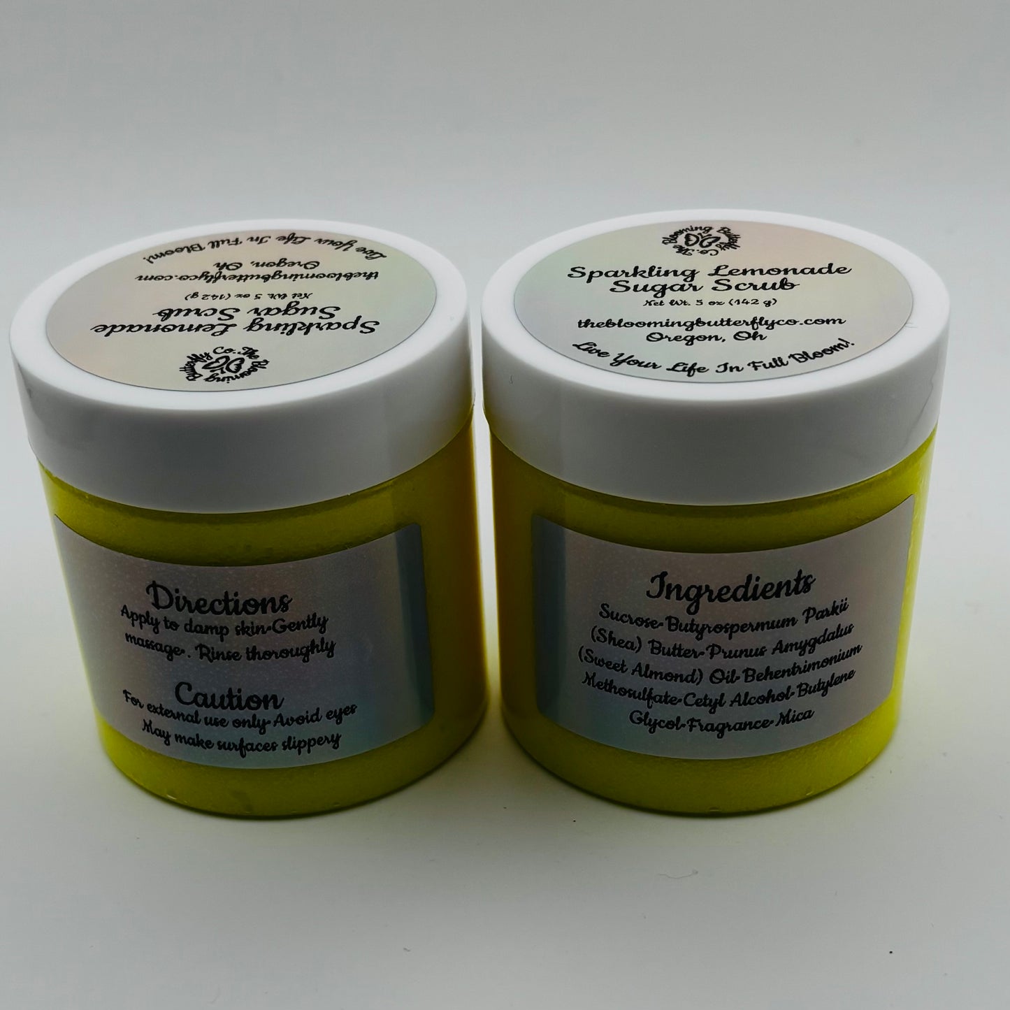 two jars of sparkling lemonade sugar scrub with labels describing directions, and ingredients by the blooming butterfly company