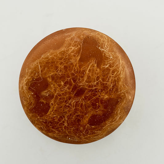 close up view of round three-inch white tea loofah soap bar infused with organically grown loofahs and shimmering bronze colored mica handmade by the blooming butterfly company