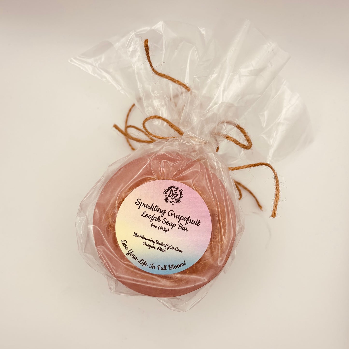 two round pink sparkling grapefruit loofah soap bars wrapped in cellophane with brown twine handcrafted by the blooming butterfly company
