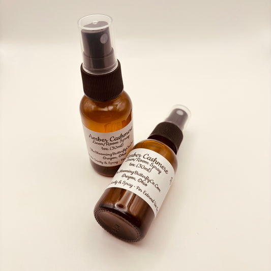 Two Amber colored spray bottles of amber, cashmere linen room spray with white label, handcrafted by the blooming butterfly company