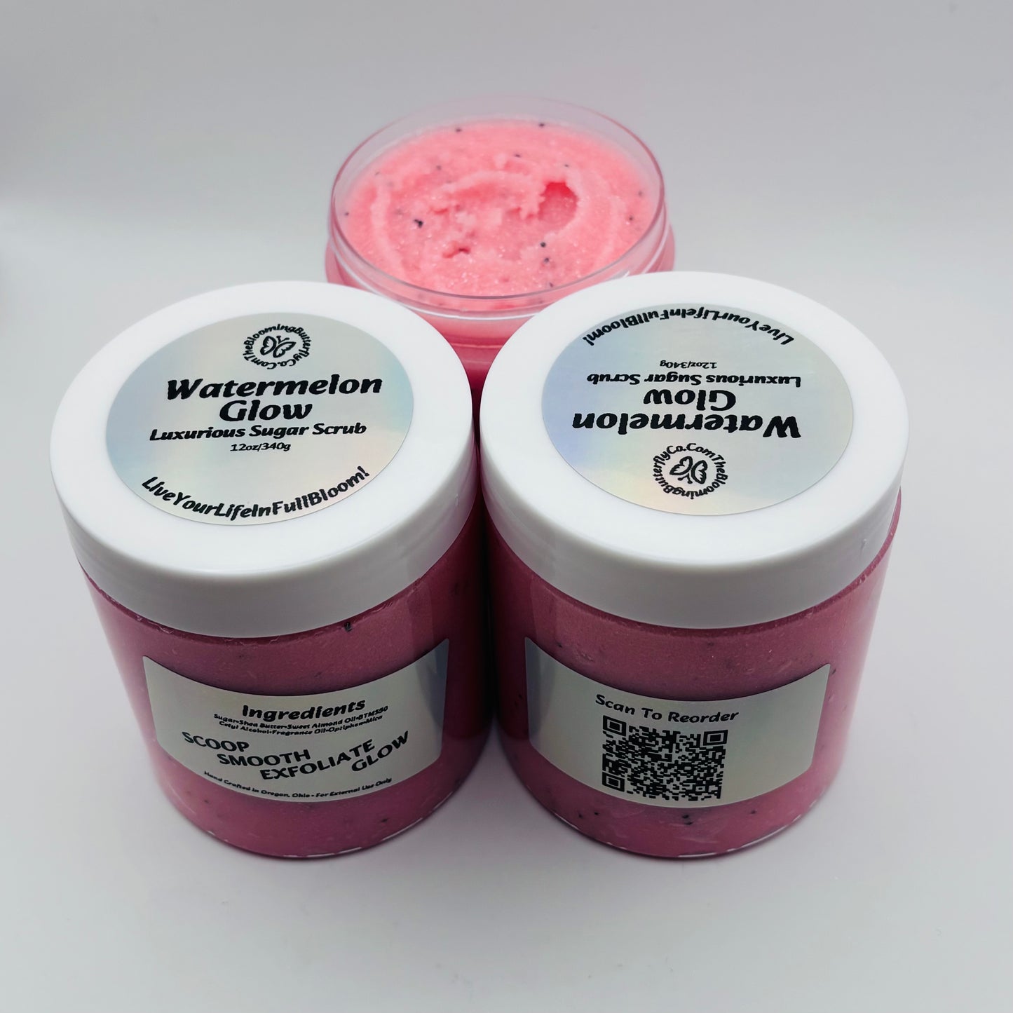Three containers of Watermelon Glow sugar scrub on a white background with holographic labels handcrafted by the blooming butterfly company