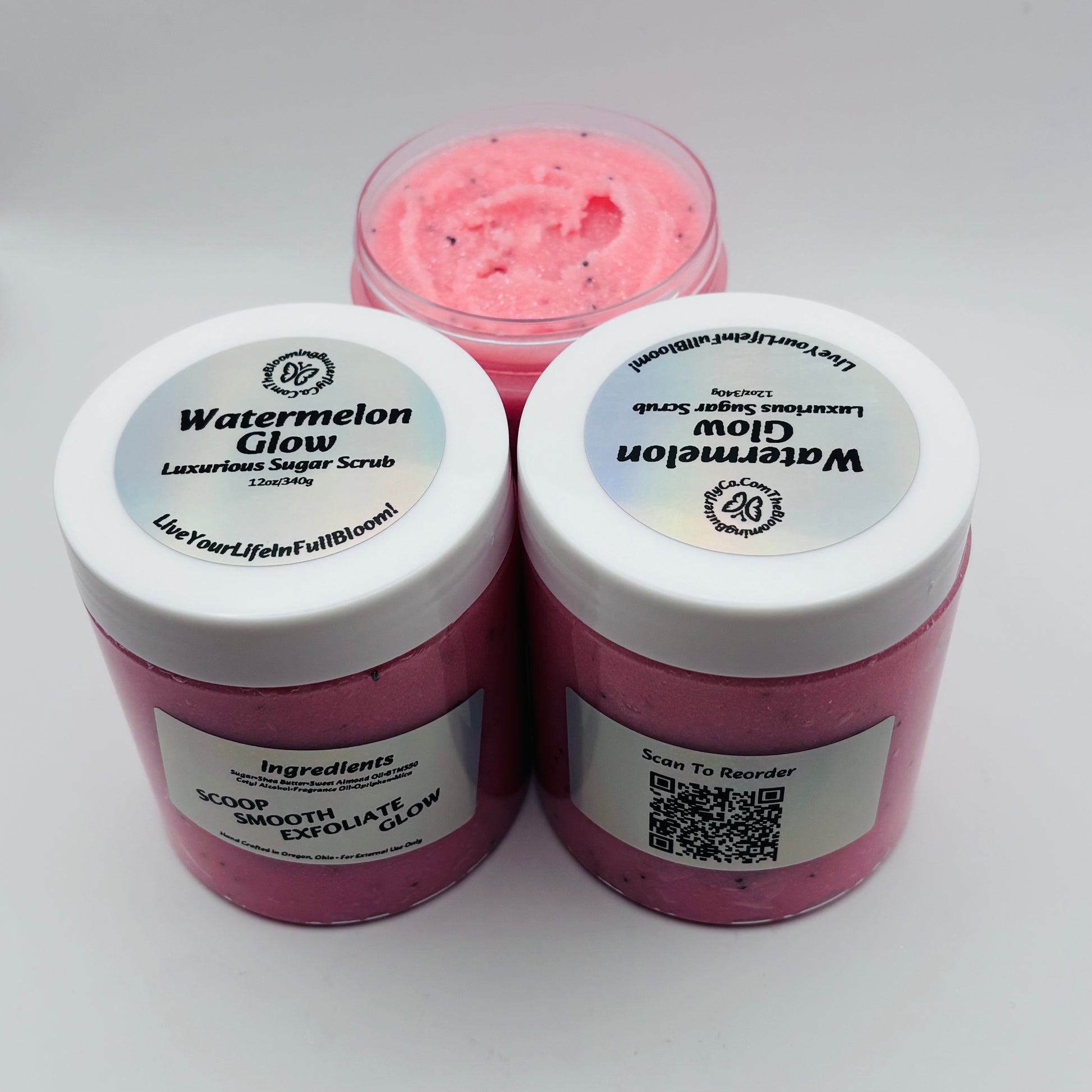 Three containers of Watermelon Glow sugar scrub on a white background with holographic labels handcrafted by the blooming butterfly company