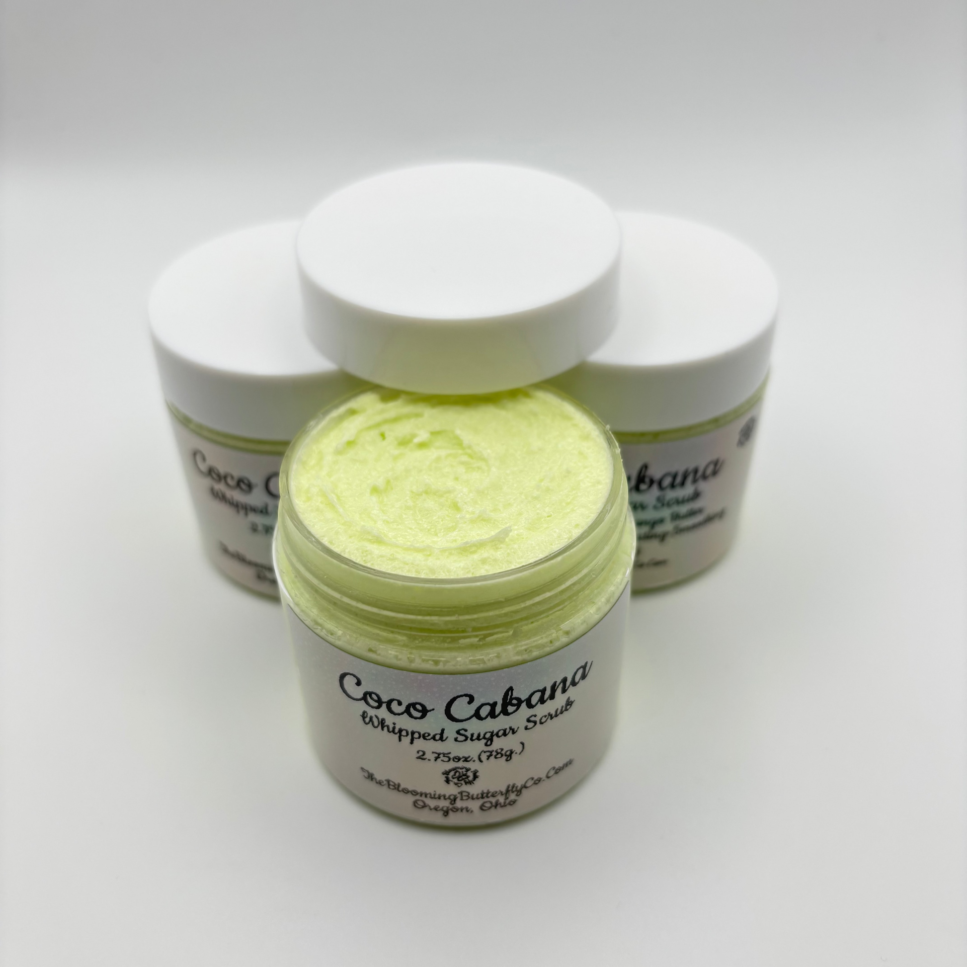 several Jars of 'Coco Cabana' whipped sugar scrub on a white background with holographic labels handcrafted by the blooming butterfly company