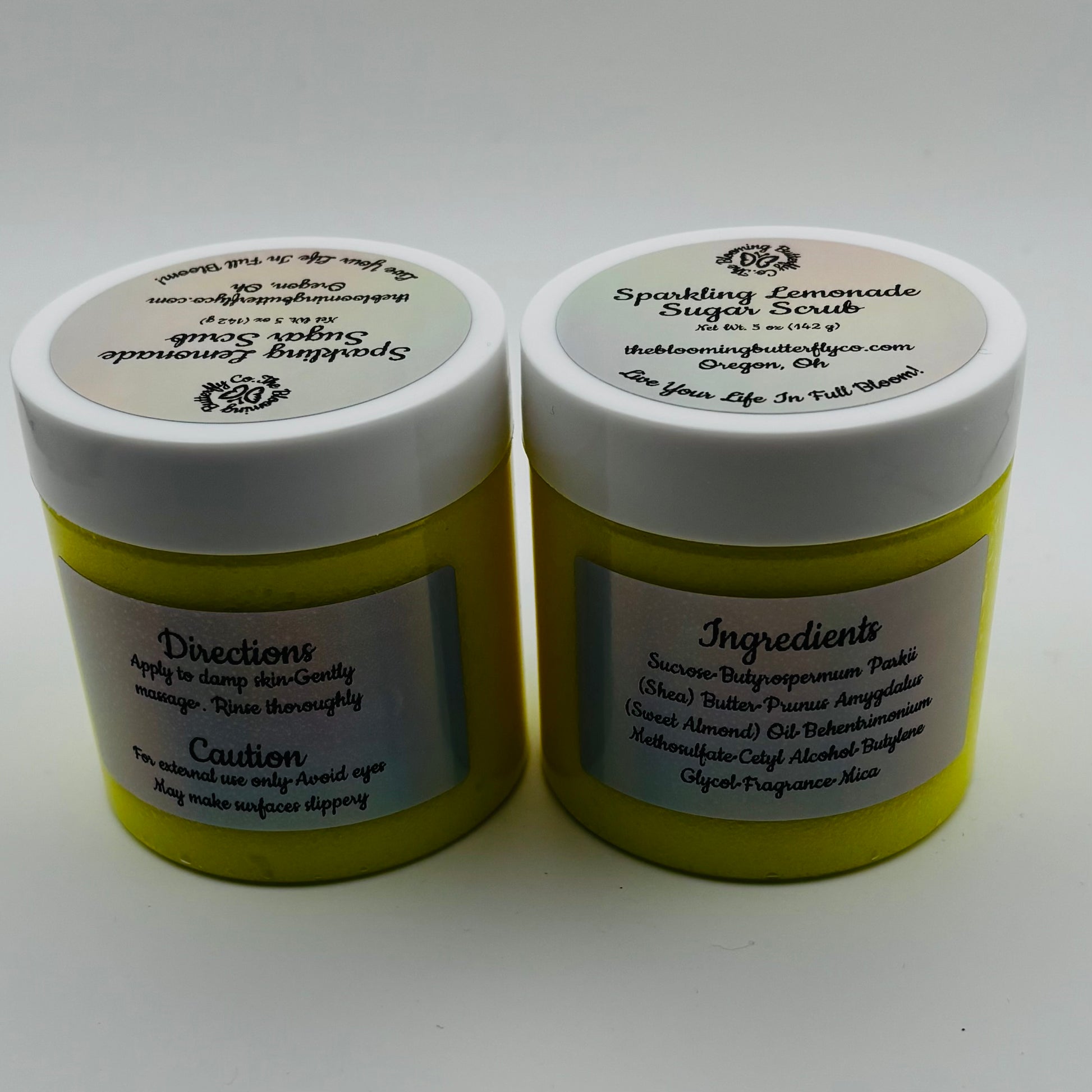 two jars of sparkling lemonade sugar scrub with labels describing directions, and ingredients by the blooming butterfly company