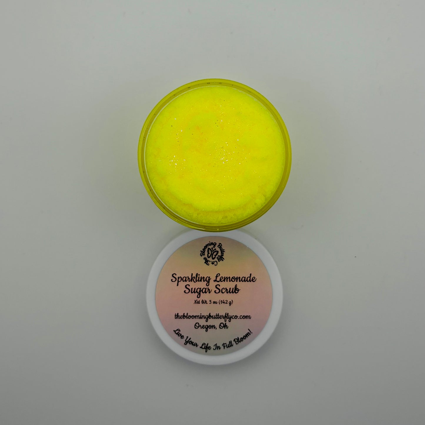 top view of creamy, scoopable bright yellow sparkling lemonade sugar scrub in a jar with a white lid by the blooming butterfly company