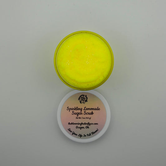 top view of creamy, scoopable bright yellow sparkling lemonade sugar scrub in a jar with a white lid by the blooming butterfly company