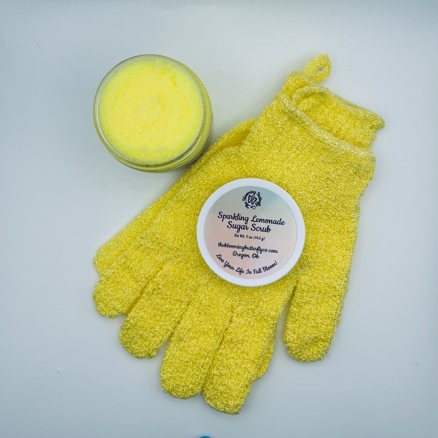 Yellow sparkling lemonade sugar scrub with shower glove and on a white background handcrafted by the blooming butterfly company