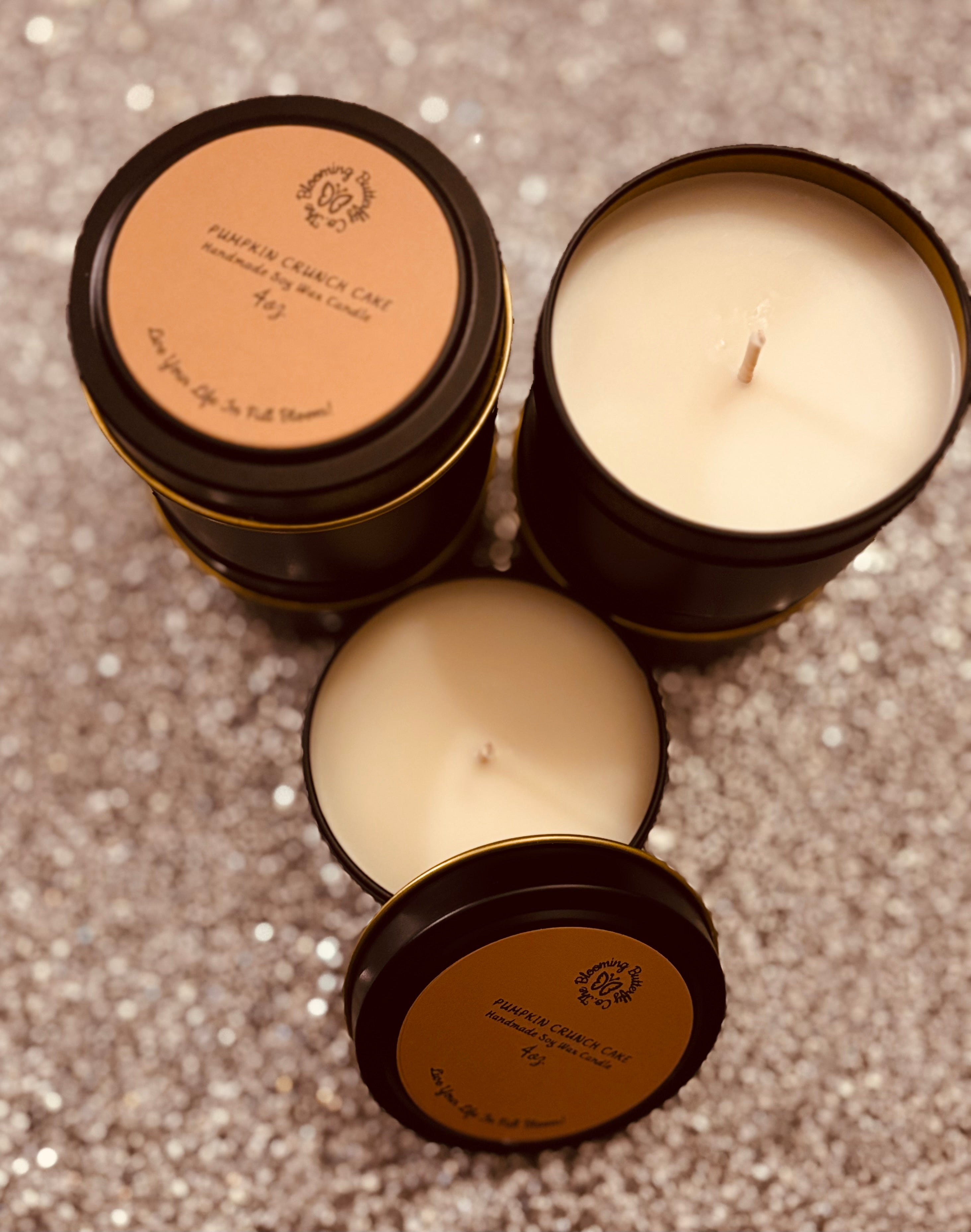 Three candles in black tins with brown labels on a glittery surface